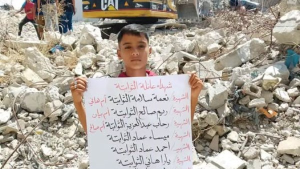 طفل يحمل لوحة شهداء عائلة الثوابتة